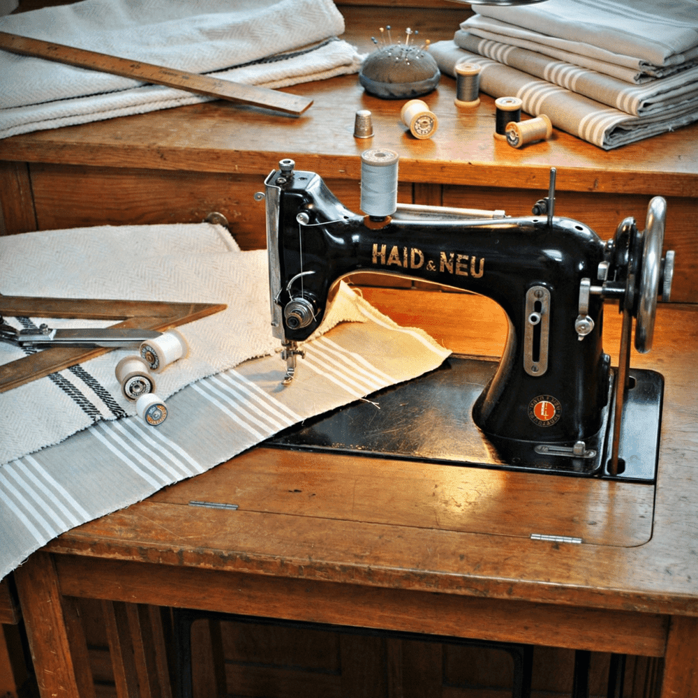 Vintage Haid & Neu sewing machine in a workshop with antique hemp fabric rolls, threads, and scissors, showcasing the handcrafted restoration process.