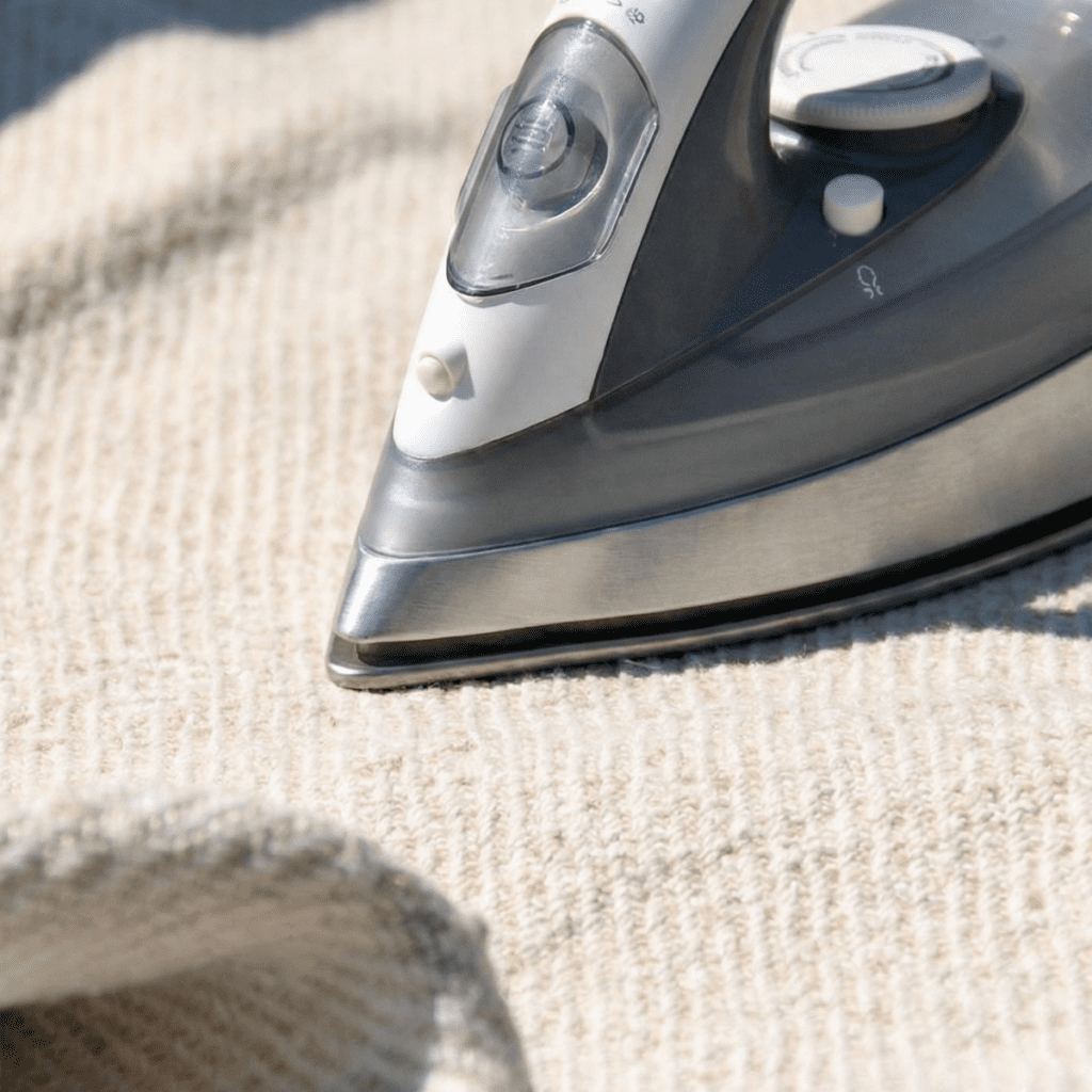 Steam iron pressing a textured antique hemp grain sack on high heat to smooth out creases while the fabric is damp.