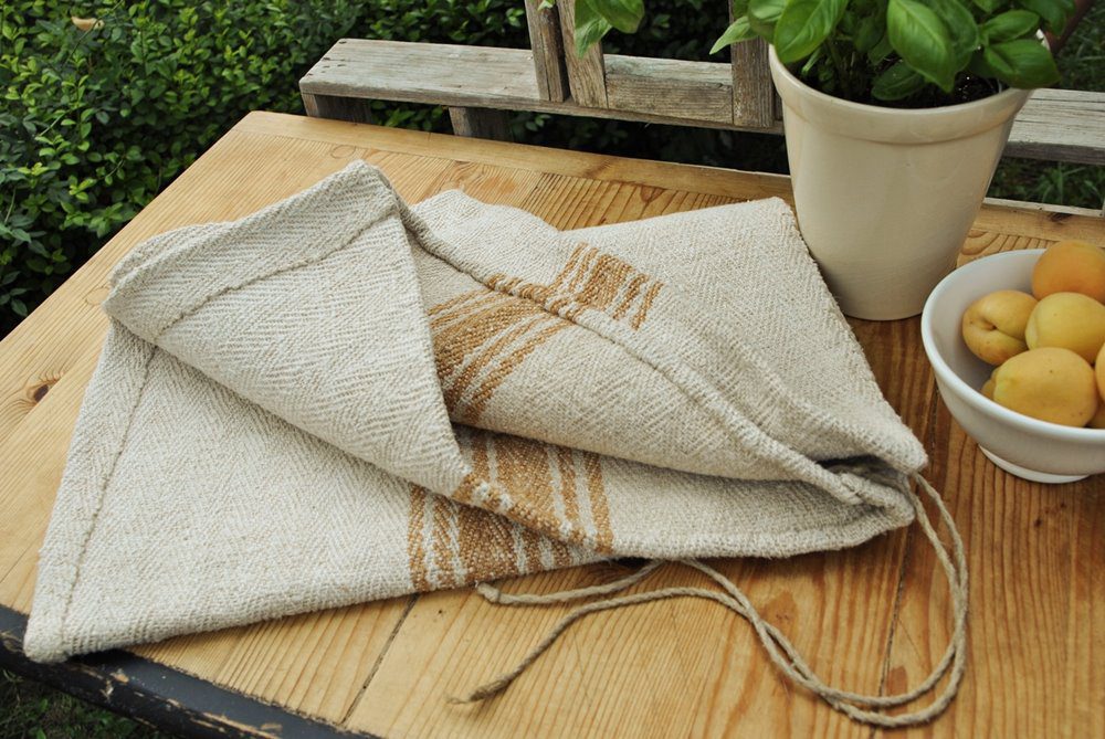 Authentic Transylvanian grain sack fabric with caramel stripes, folded on a rustic wooden table next to a bowl of apricots.