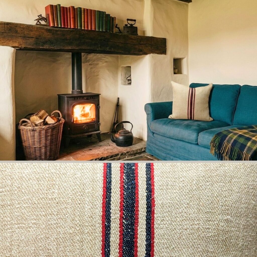 Antique grain sack cushion cover with red and navy stripe on teal sofa beside cast iron wood burner in English cottage interior with whitewashed walls and oak beam