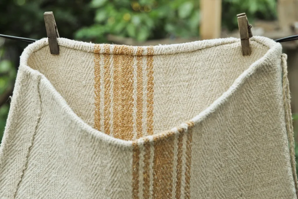 Antique grain sack hanging on clothesline outdoors, unbleached natural hemp in warm yellow-oatmeal tone, caramel woven stripes, 4-shaft twill weave, Transylvania