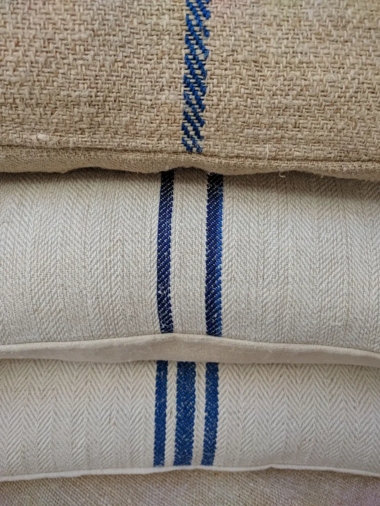 Three antique grain sack pillows stacked showing stripe variety, plain weave coarse hemp top, herringbone twill middle and bottom with different blue stripe widths and spacings, Transylvania