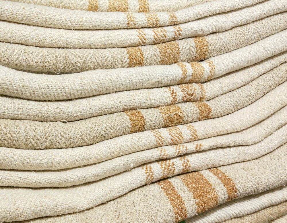 Close-up detail of stacked vintage grain sacks showing the distinct hand-woven caramel stripes used as family signatures.