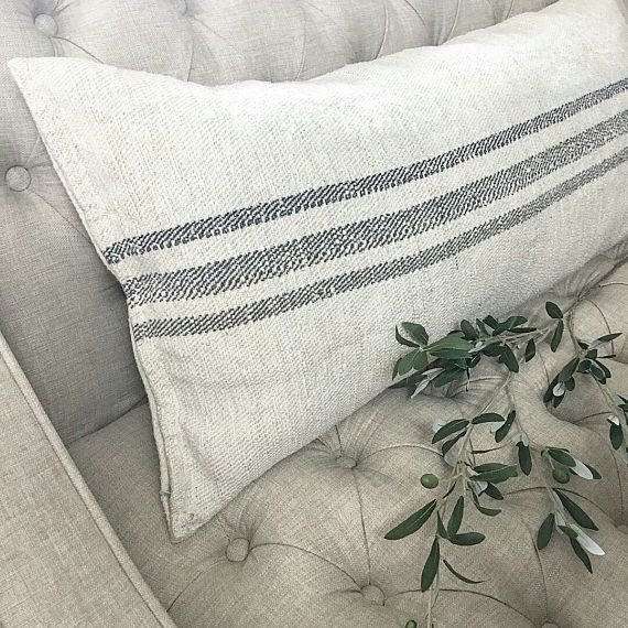 Antique grain sack lumbar cushion on grey tufted sofa with olive branch, natural stripe hemp textile, interior styling