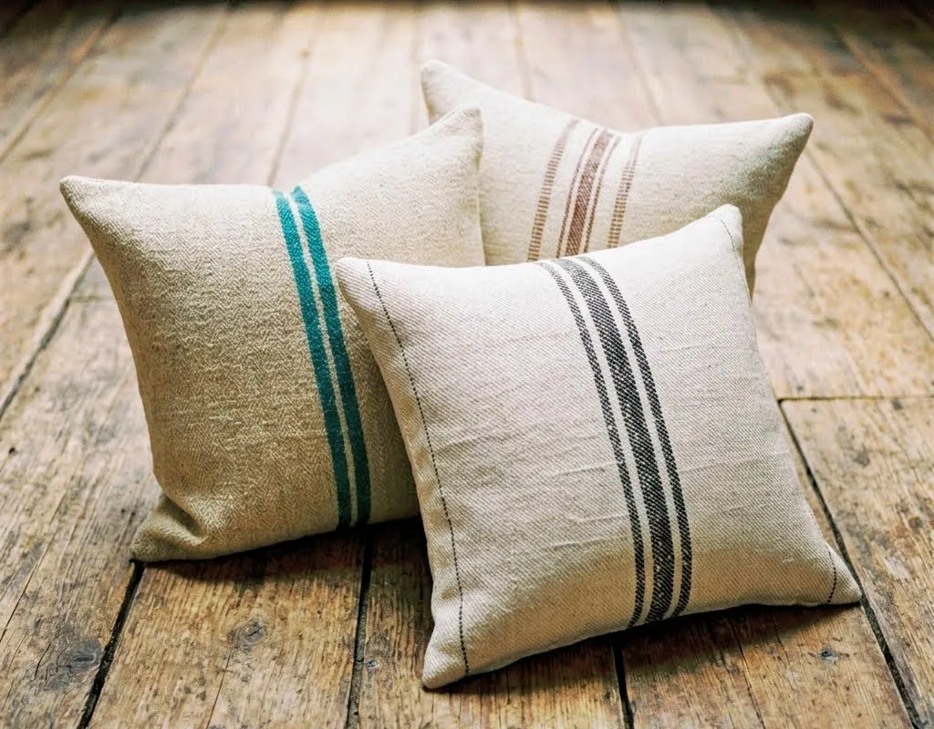 Collection of antique Transylvanian grain sack pillow covers showing varied stripe patterns in cream, grey, indigo and rust tones, each piece unique and irreplaceable